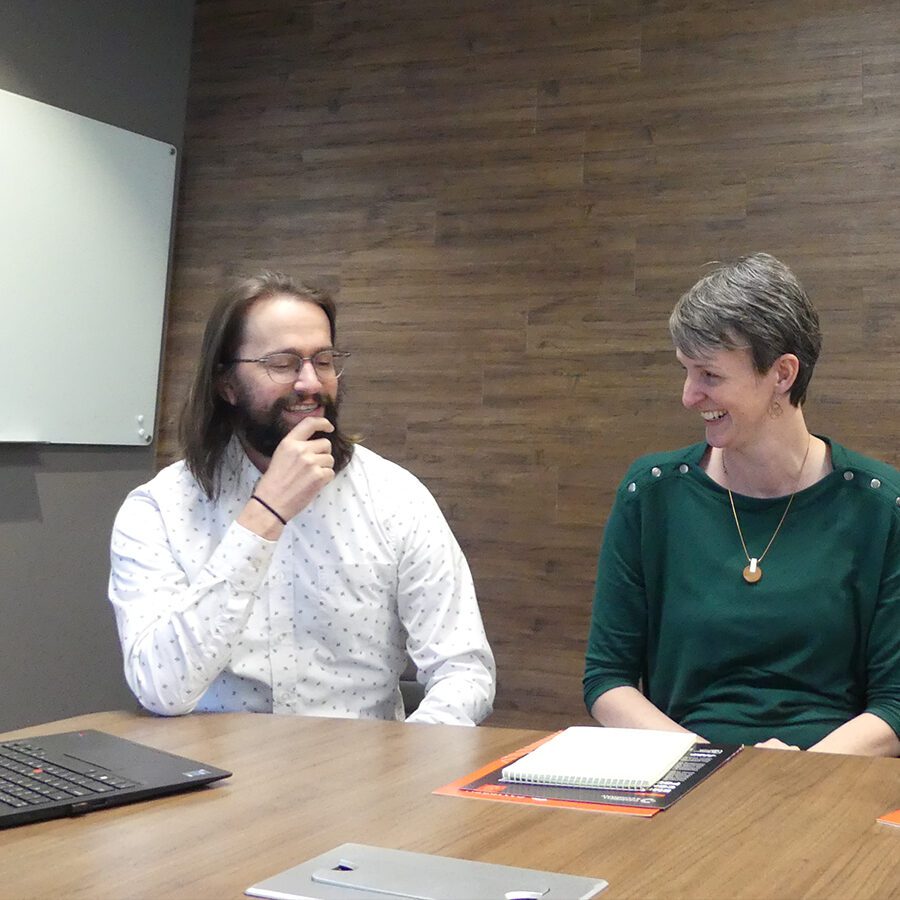 Man and woman sitting in a conference room, smiling.