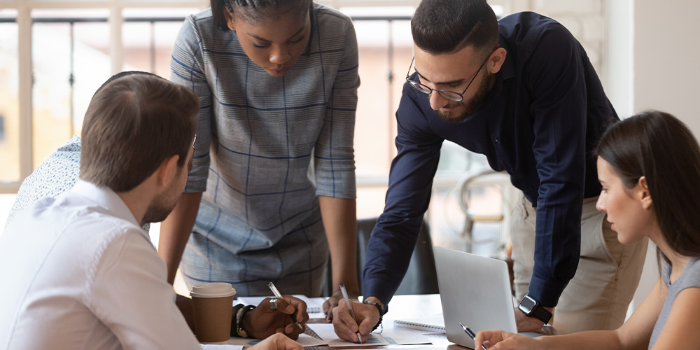 Group of people gather around desk and review paperwork.