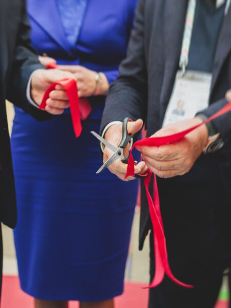 Process of cutting the red ribbon during the grand opening of the new shopping center mall building, opening of exhibition, close up view of red ribbon with people around