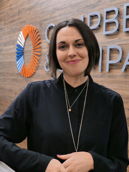Woman standing, her elbow on a countertop, and smiling